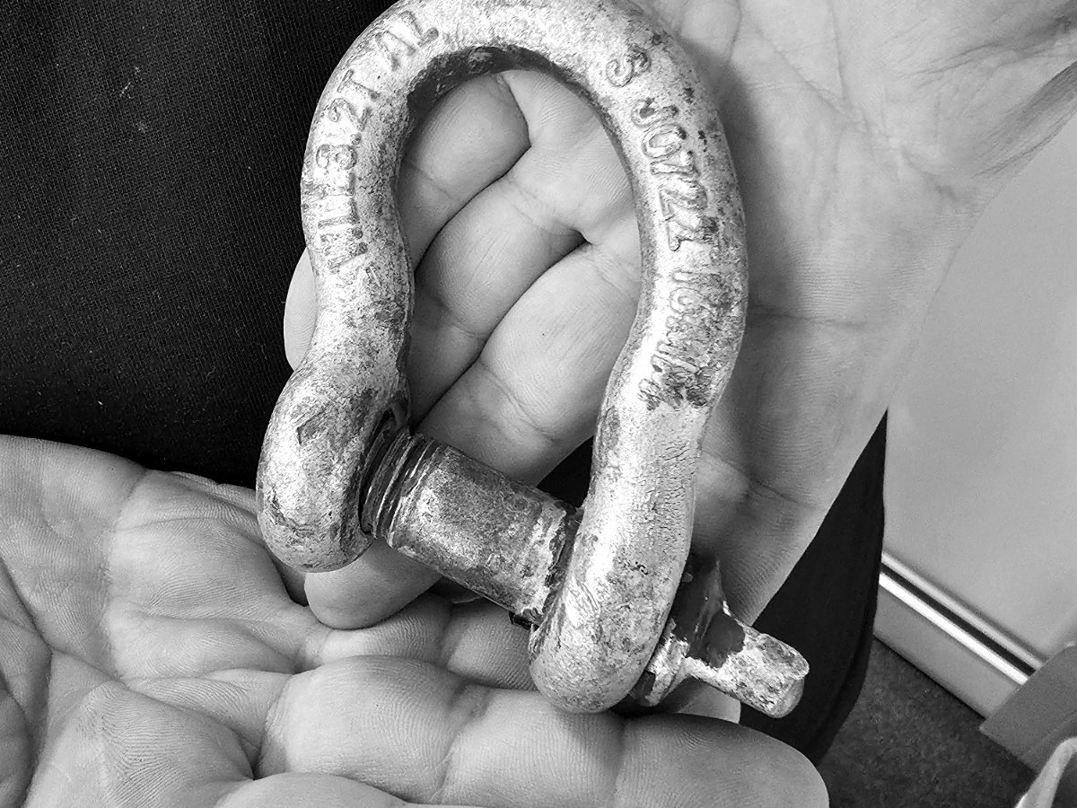 Galvanised bow shackle held in a hand, showing the stamped markings on the body and a screw pin with a blue thread band